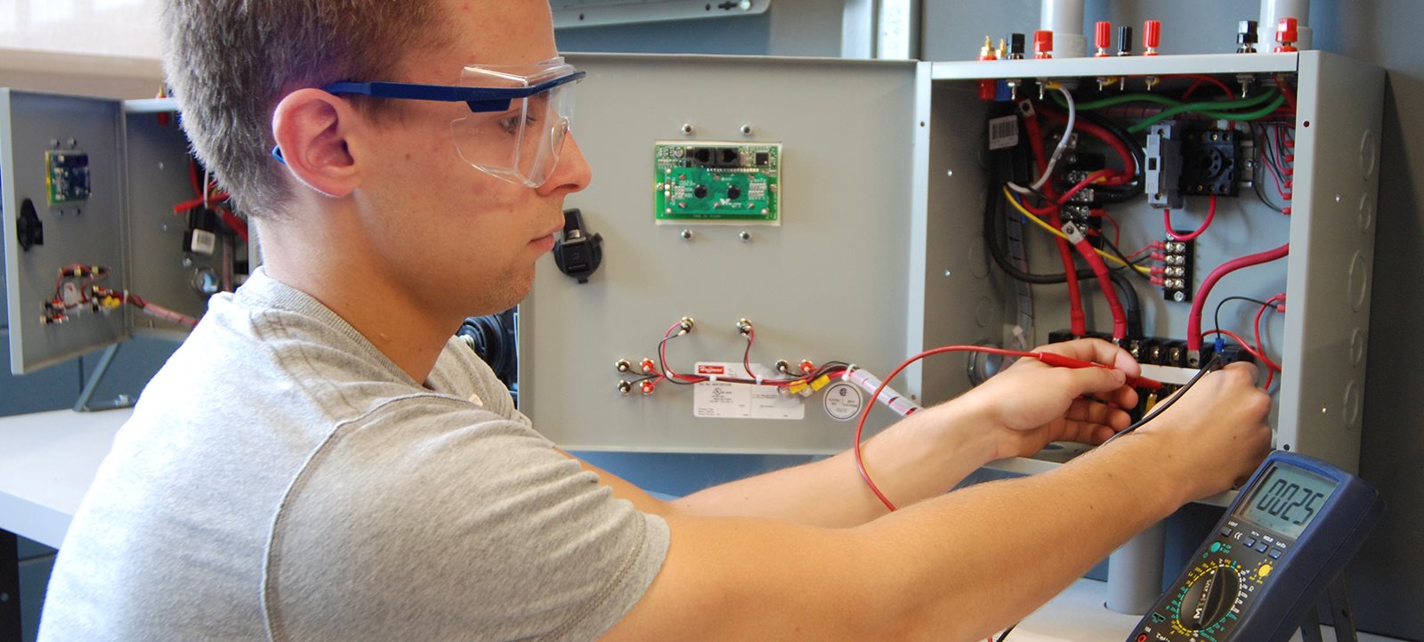 Jeune homme avec lunettes de protection qui travaille avec dans un boite comprenant des fils électriques 