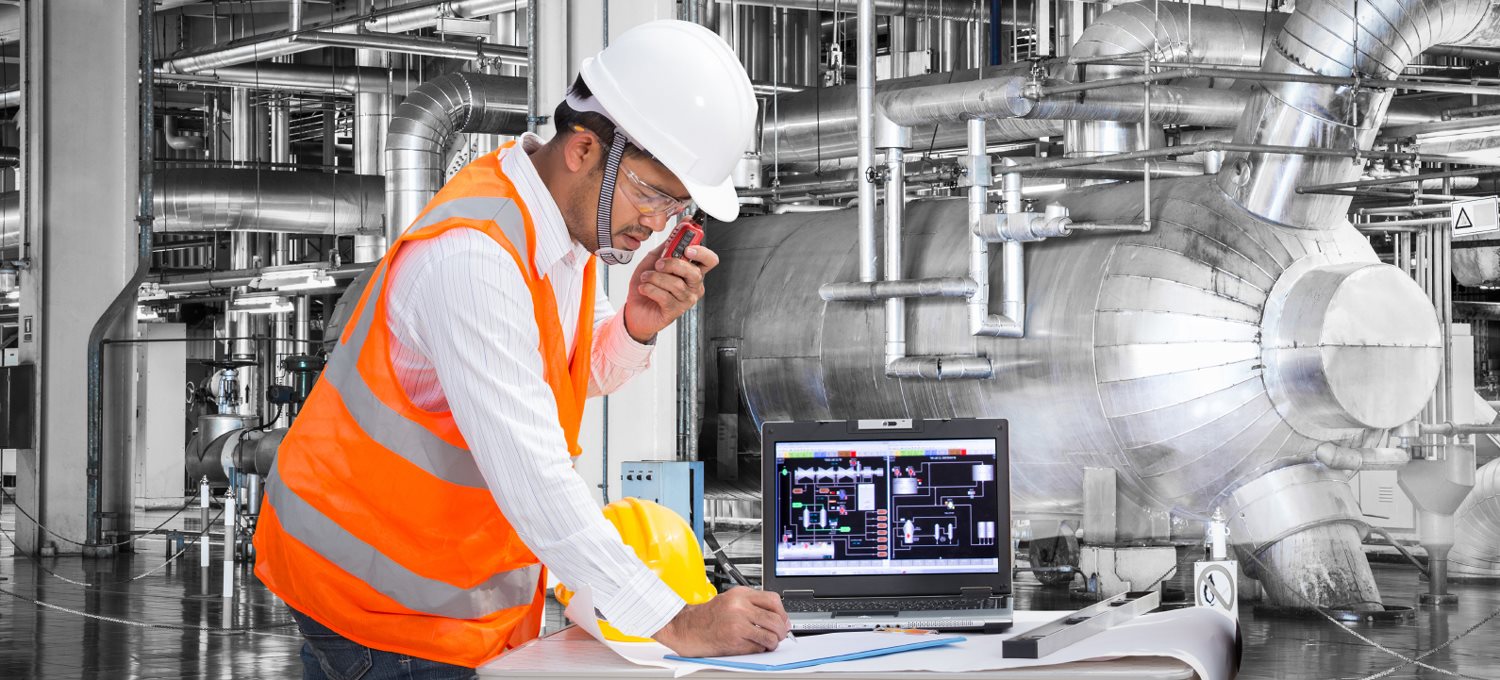 Homme portant un dossard et un casque de construction devant des conduits de ventilation