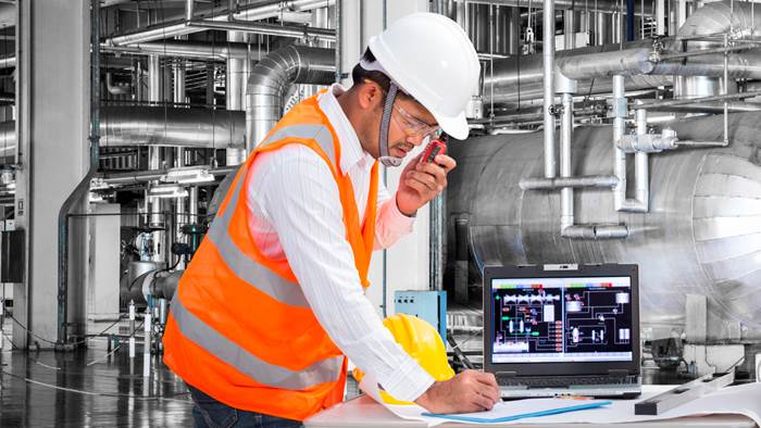 Homme portant un dossard et un casque de construction devant des conduits de ventilation